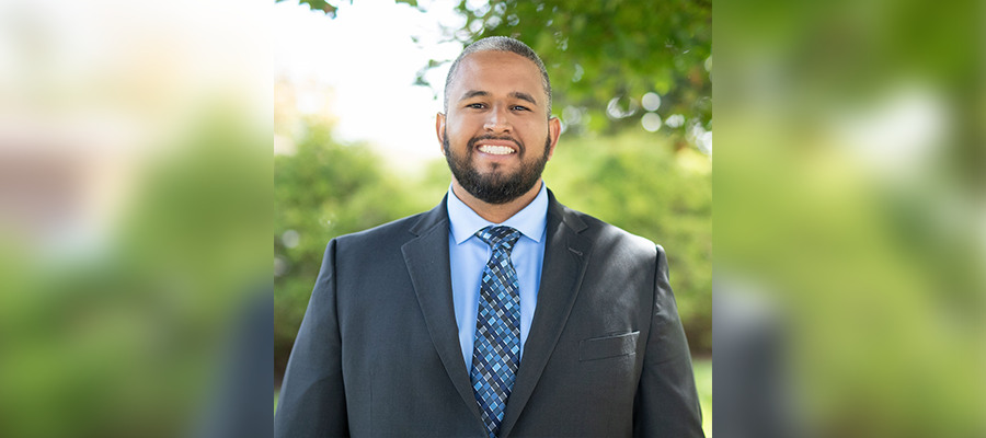 Raul E. Perez Jr., Safety Manager at ACRT Pacific, smiling in a professional headshot outdoors, wearing a dark suit, light blue shirt, and patterned blue tie. Posted for Employee Ownership Month.