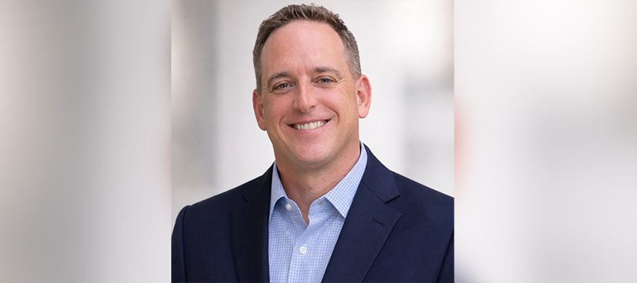 Headshot of Michael Hedrick smiling, wearing a navy blazer and light blue shirt against a neutral background.